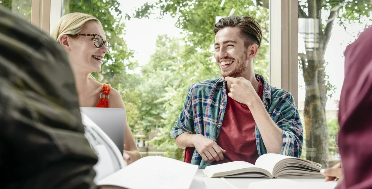 Group of happy college students reading in library and having fun, man with facial hair and hand on chin, smiling