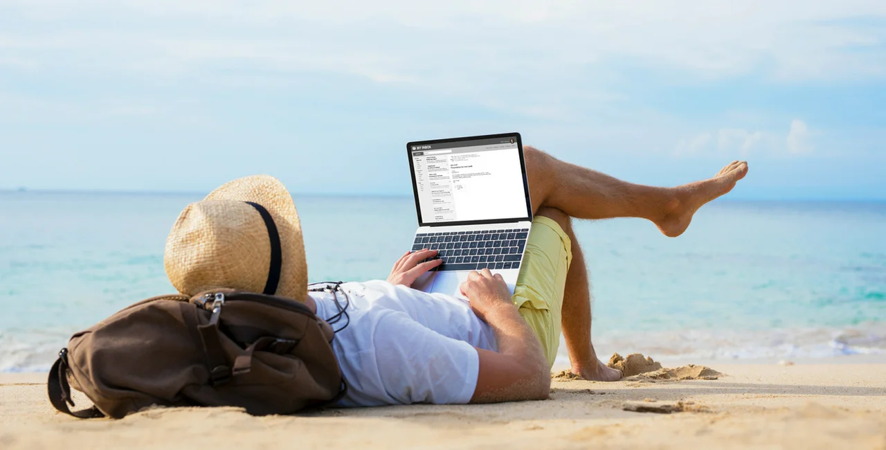 Unrecognizable male reading email on laptop while relaxing on beach