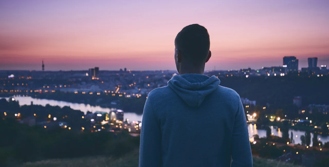 A young man watches the sunrise over Prague's skyline