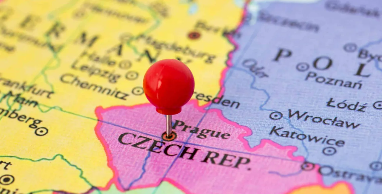 Round red thumb tack pinched through city of Prague on Czech Republic map