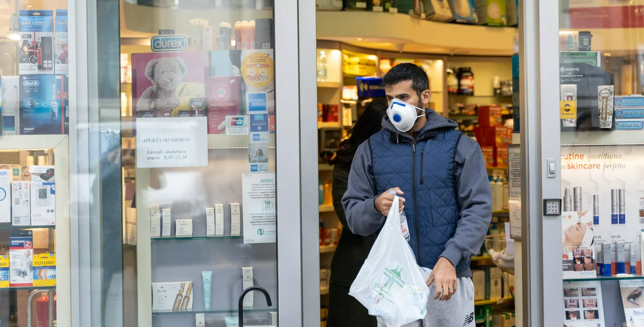 A man wearing a face mask walks out of a pharmacy in Milan, Italy during the coronavirus epidemic. Illustrative photo via iStock / Denis Sokol