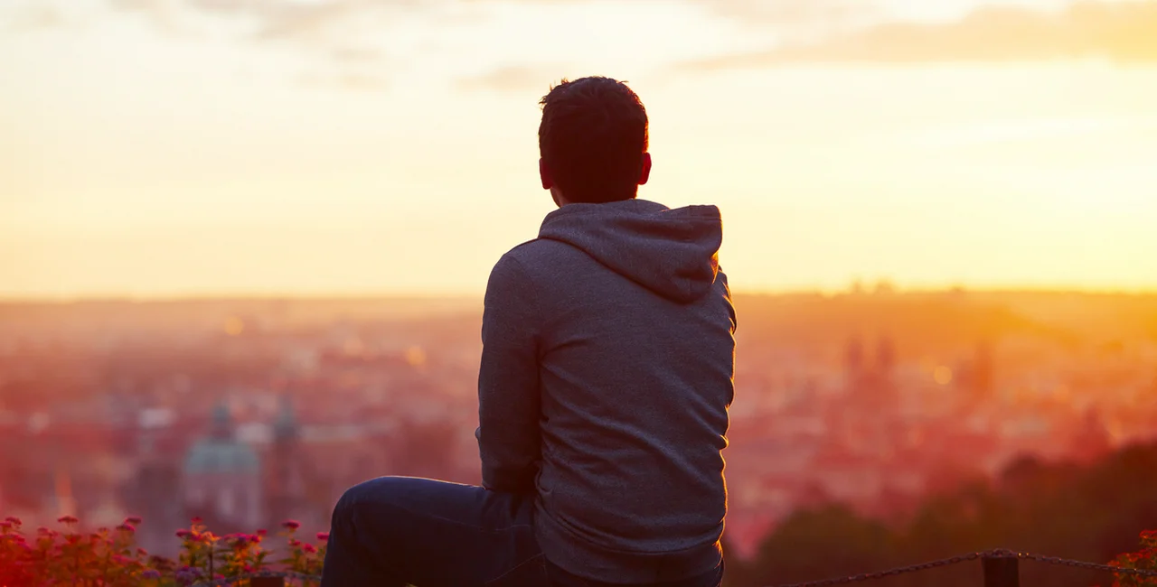 A young man watches the sunrise in Prague via iStock.com / Chalabala