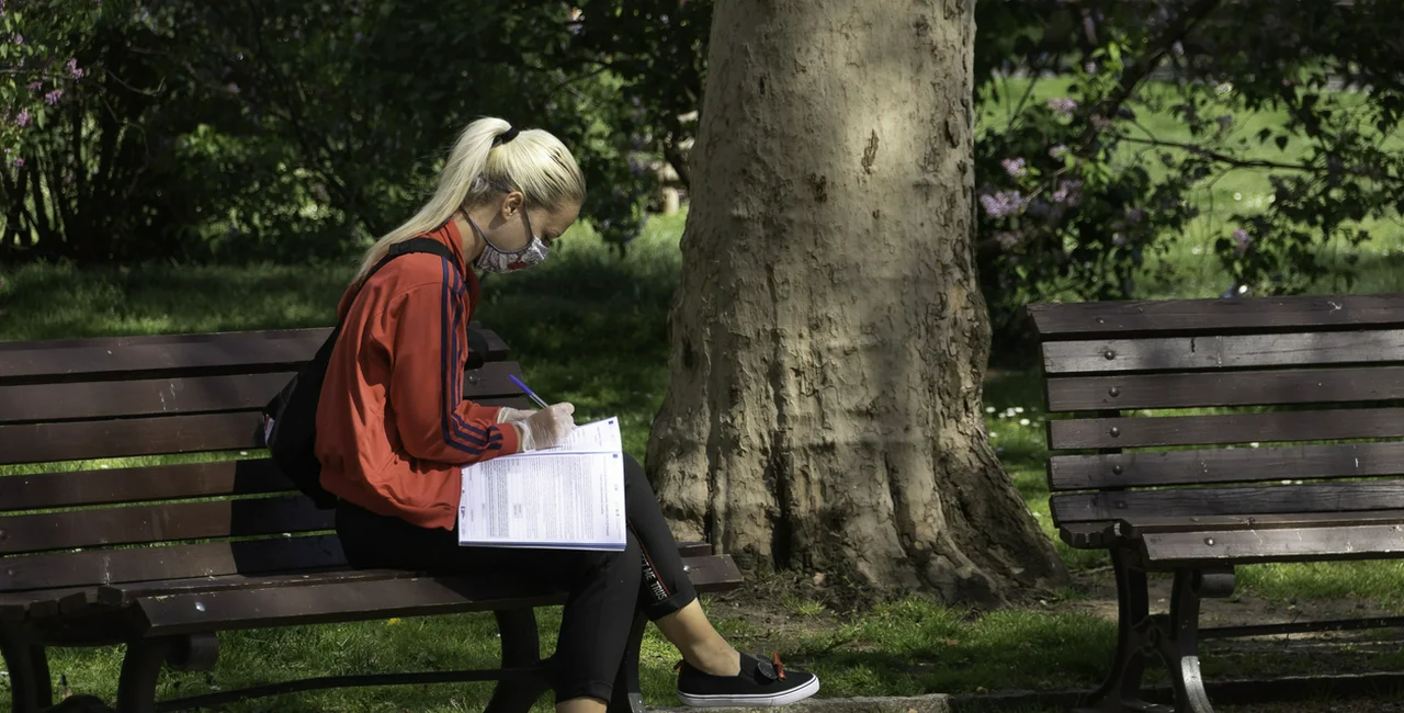 Young woman on a park bench in Prague filling out paperwork before taking a COVID-19 test via iStock / Albertem