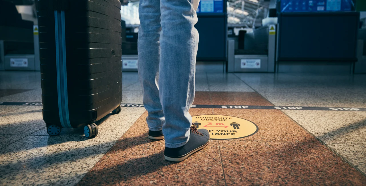 Traveler standing above a social distancing sign at Prague Airport via iStock / Chalabala