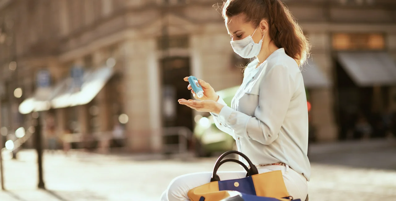 Woman wearing a face mask and using hand sanitizer on the streets of Prague via iStock / CentralITAlliance