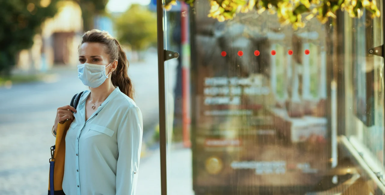 Woman wearing a face mask waits at a Prague bus stop via iStock / CentralITAlliance