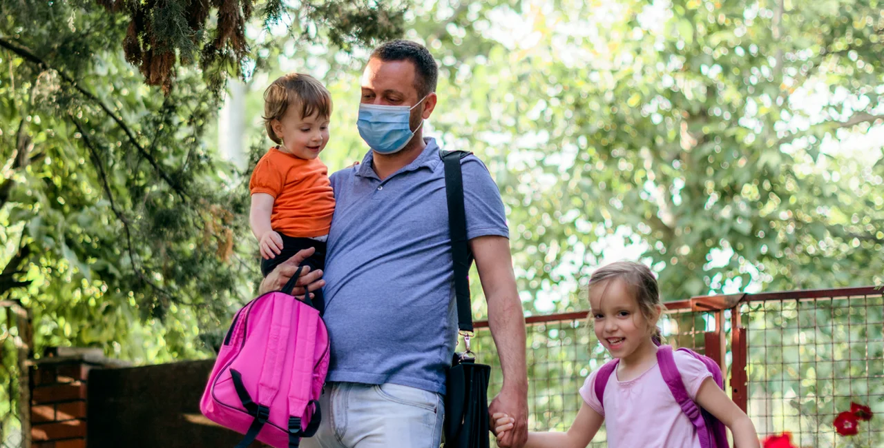 Father wearing a face mask brings his children to school via iStock / StockPlanets
