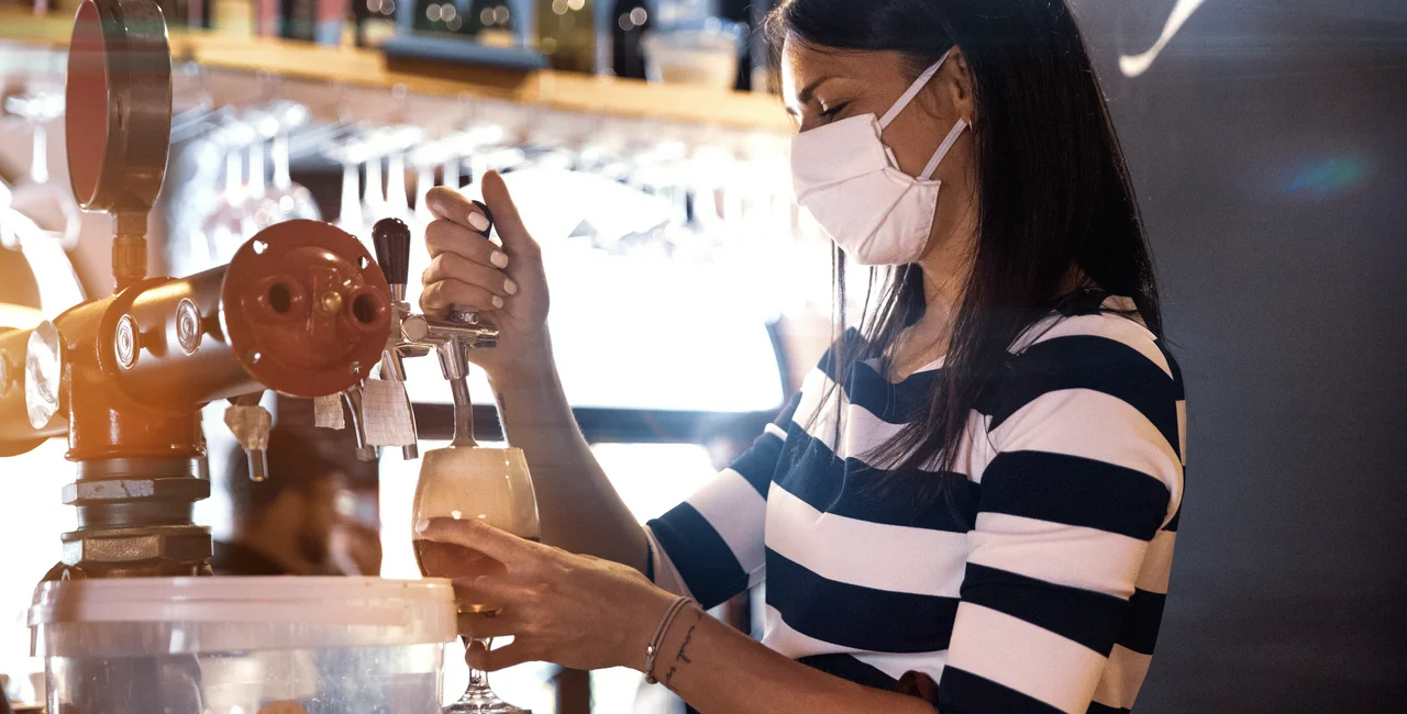 Bartender wearing a face mask pours a glass of beer via iStock / LeoPatrizi