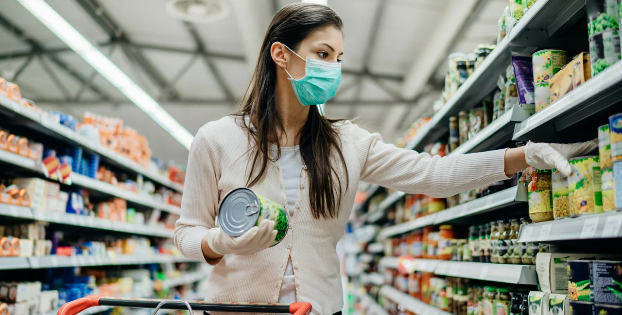 A woman shops for food while wearing a face mask via iStock / eldinhoid