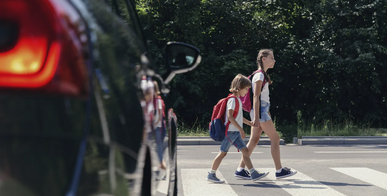 Children crossing the street in front of a car via iStock / KatarzynaBialasiewicz