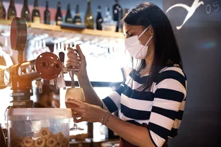 Bartender wearing a face mask pours a glass of beer via iStock / LeoPatrizi