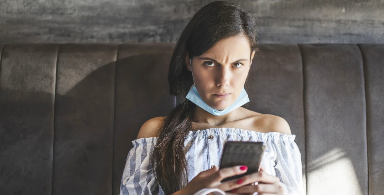 Woman with face mask around neck via iStock / DjordjeDjurdjevic