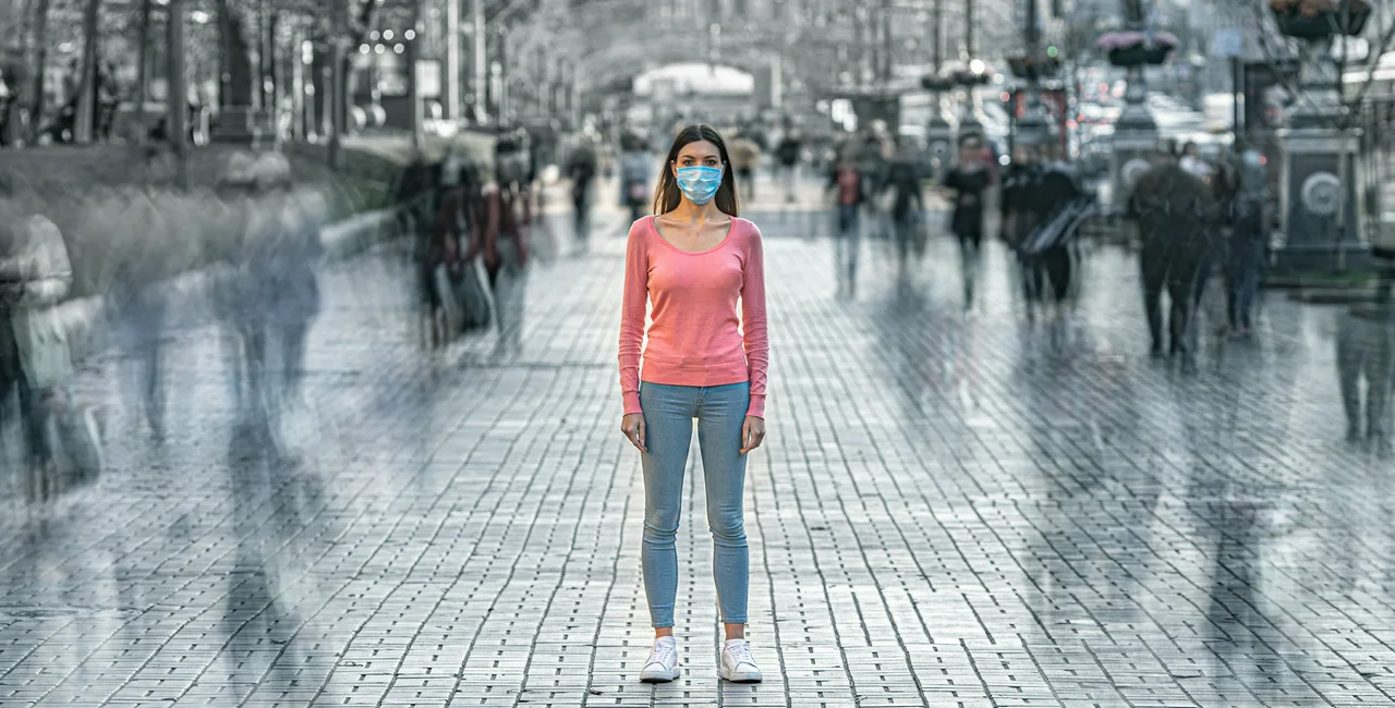 Woman in mask on street, blurred passersby. (photo: iStock /  Viacheslav Peretiatko)