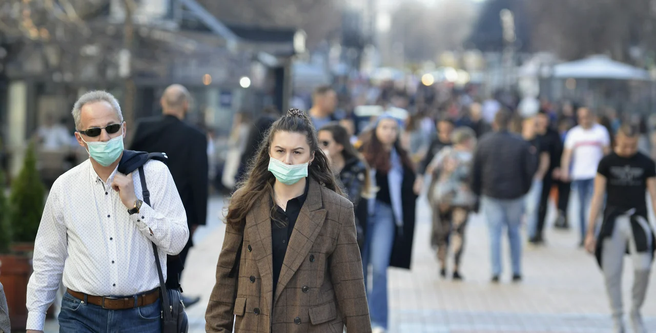 People in masks walking down street. (photo: iStock / JordanSimeonov)