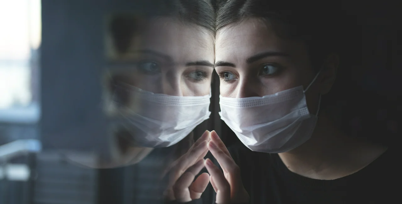 Woman looking out window with mask on. (photo: iStock / Xesai)