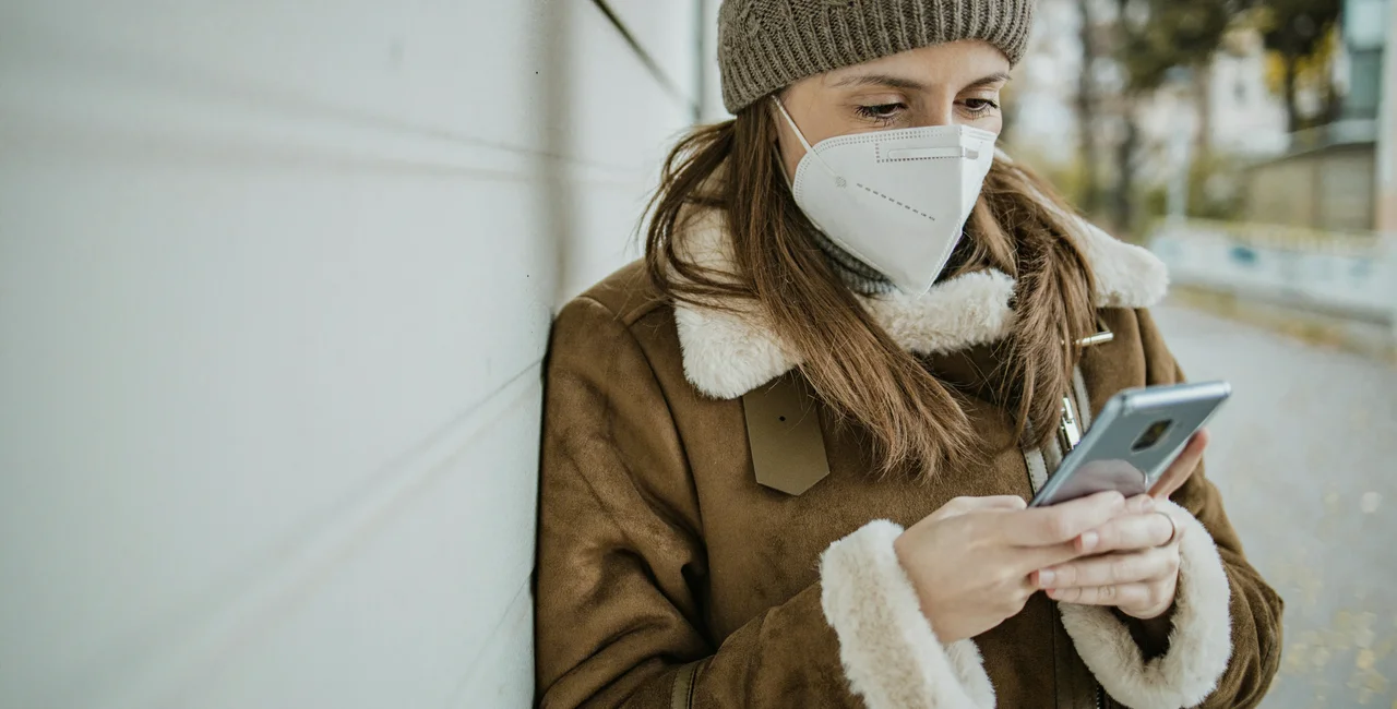 Woman wearing face mask and us9ing phone via iStock / blackCAT