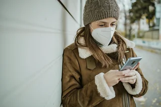 Woman wearing face mask and us9ing phone via iStock / blackCAT
