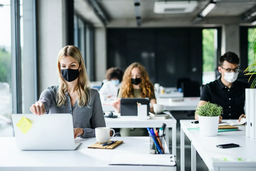 Young people in office wearing face masks via iStock / Halfpoint
