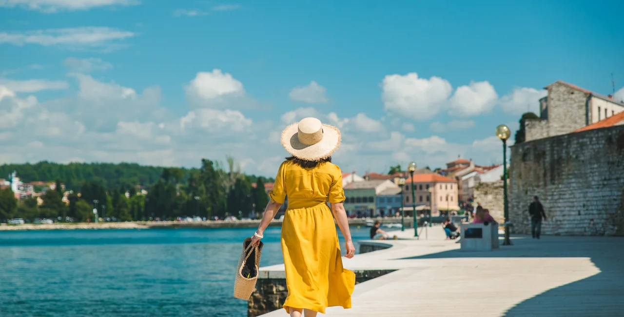 Woman walking by the sea in Croatia in a yellow sundress. (Photo: iStock, Vera_Petrunina)