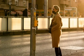 Woman with mask waiting to cross the street at sunset in Prague. (Photo: iStock, Humanitarian photographer working for UN Agencies)
