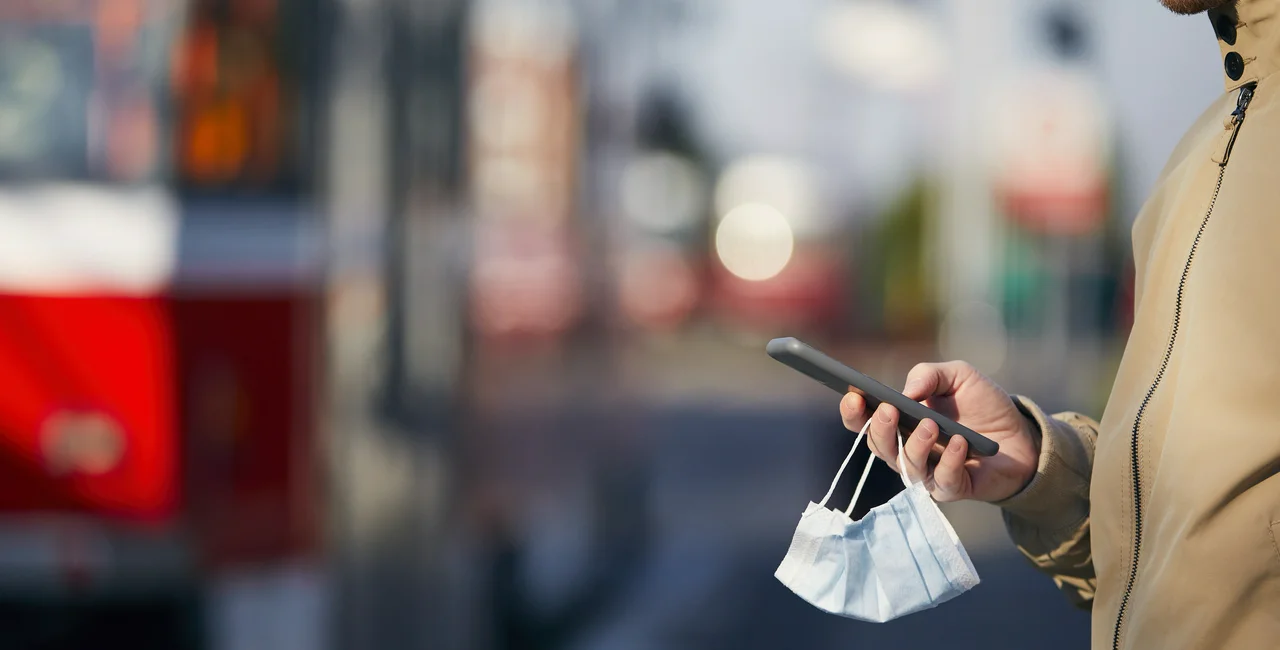 Young man with face mask in hand using smart phone during waiting for tram. (Photo: iStock,