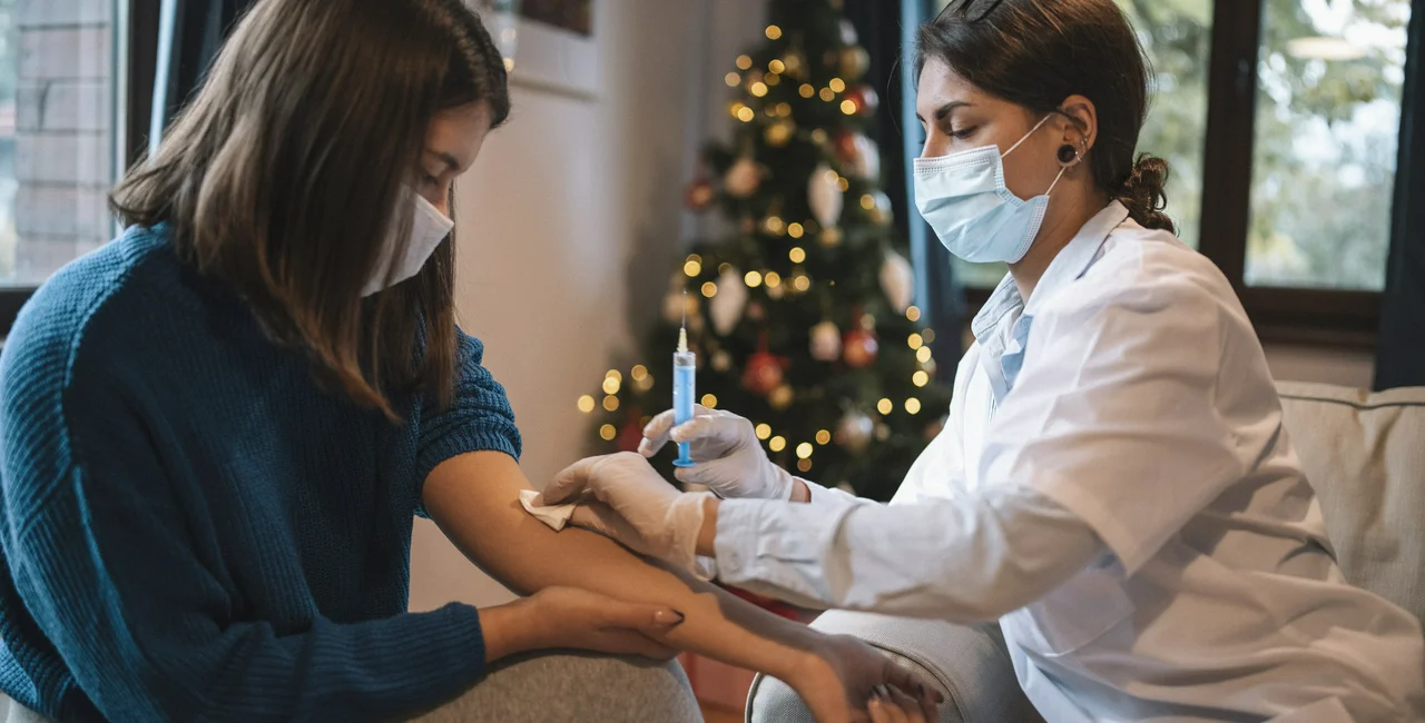 Doctor administers Covid-19 vaccine with Christmas tree in background. Photo: iStock /