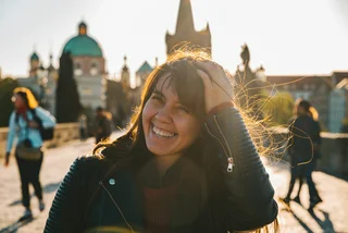 iStock-1174934338 Vera_Petrunina Woman portrait at sunrise with messy hair due to wind stock photo woman happy charles bridge nice