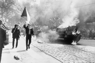 People carry the Czechoslovak flag past a burning tank in Prague. Photo CIA, public domain.