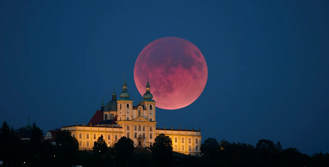 Total lunar eclipse with a glowing red moon rising above the illuminated baroque Pilgrimage Basilica of Our Lady of the Holy Hill. Blood moon rising over baroque church in Olomouc. Photo: Martin Mecnarowski/Shutterstock