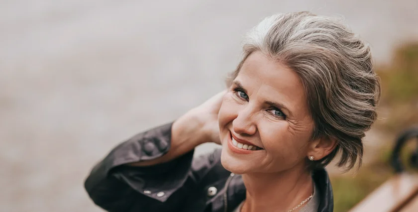 A friendly and professional lifestyle portrait of a female life coach smiling warmly outdoors.