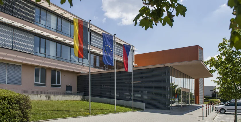 The main entrance of the Deutsche Schule Prag with the german, EU and czech flags waving next to it on the school's lawn.