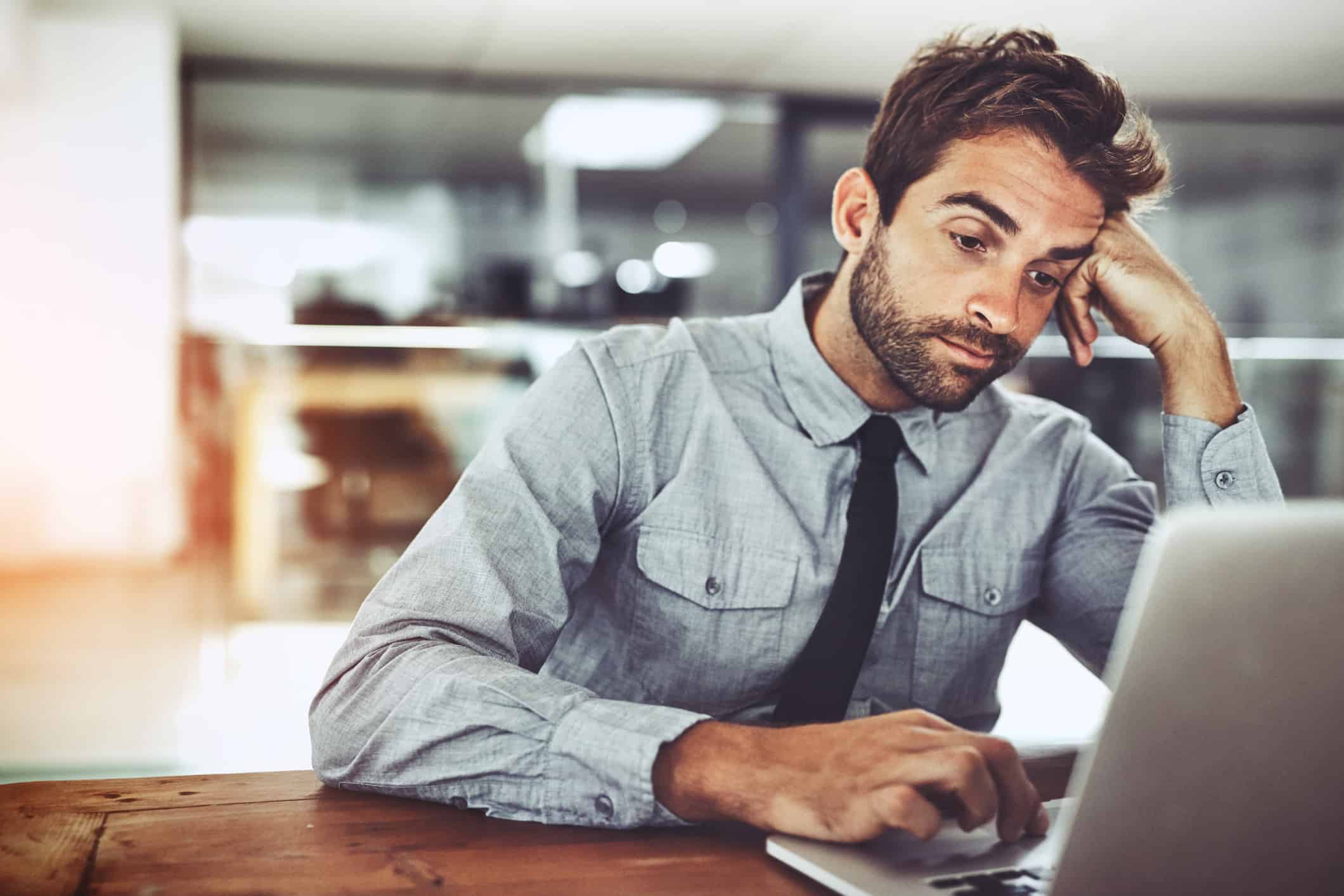 Shot of a handsome young businessman looking bored while working on a laptop in an office