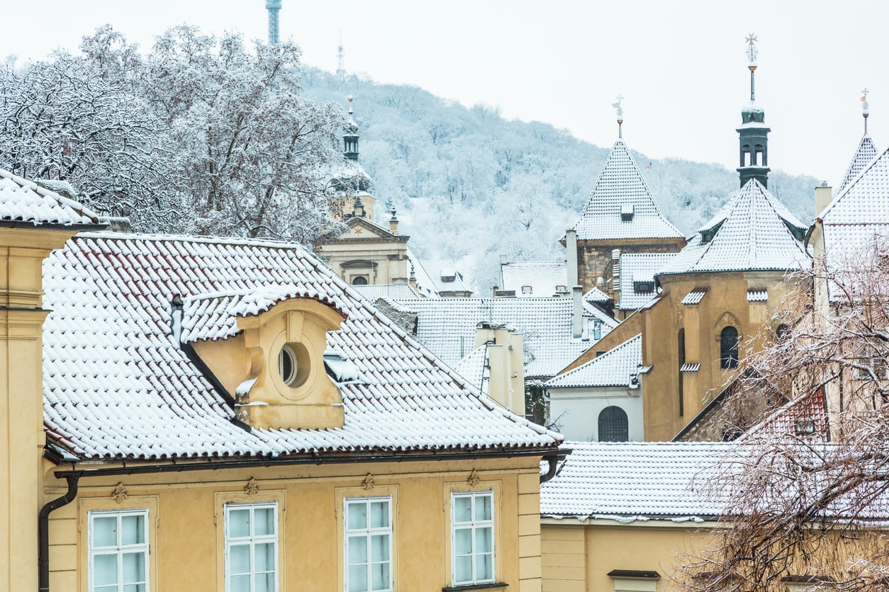 Snow-covered tiled roofs of  Malá Strana in front of the Petřín Hill and Tower.