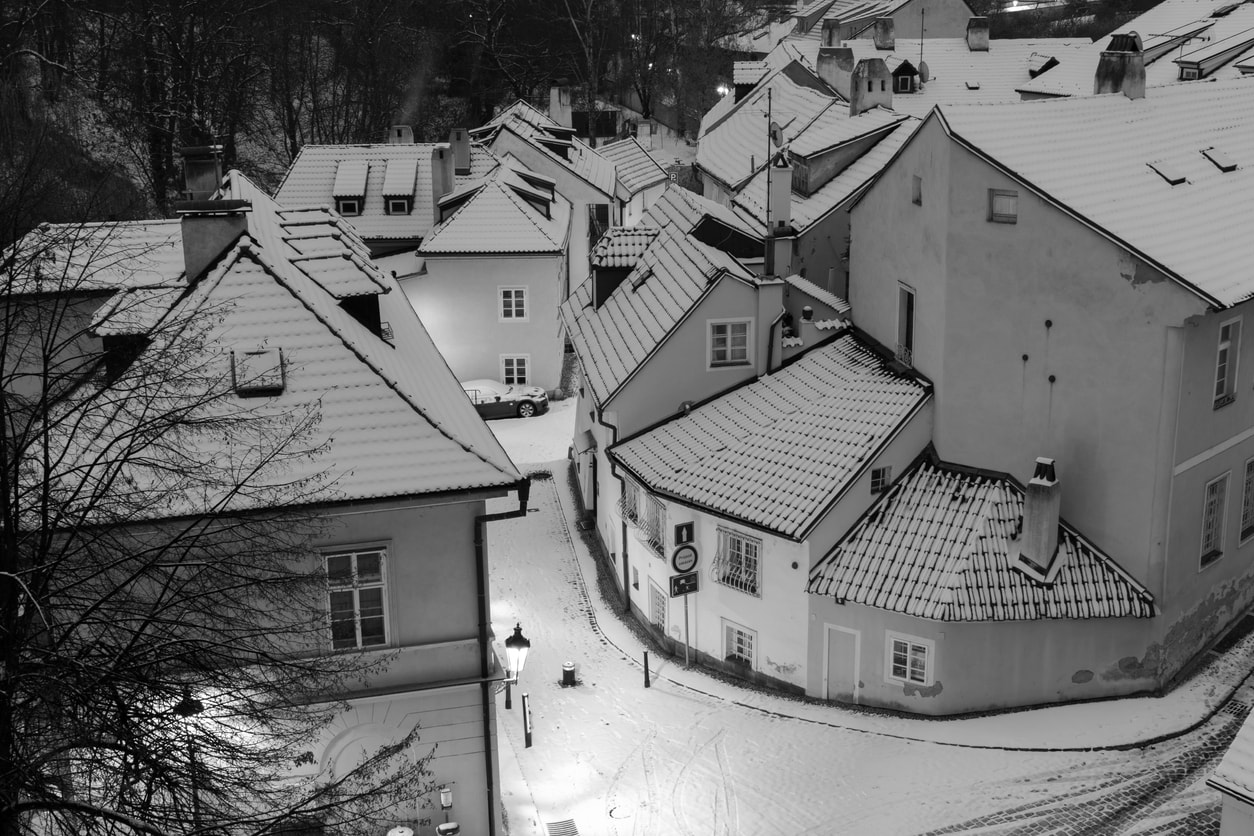 Snow-covered streets and roofs in the romantic Nový Svět district in central Prague, illuminated by vintage street lamps.