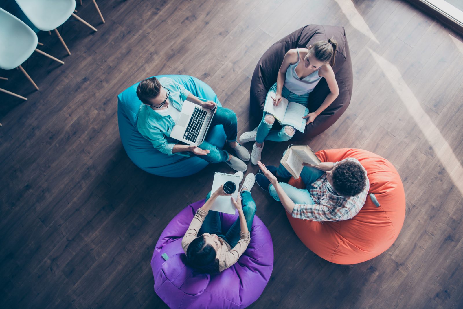 High top angle view of diversity stylish and modern hipster youngster sit in colorful armchairs on the wooden floor work together on the task sit classmates chair bag