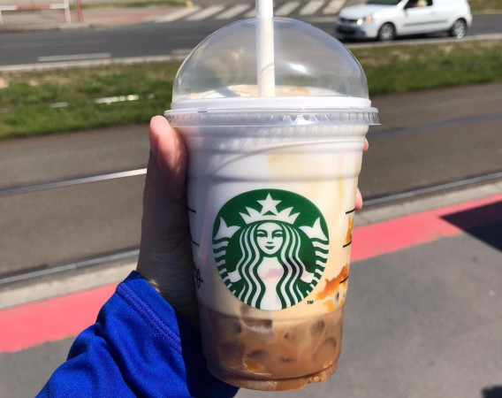A hand holding a Starbucks Cloud Macchiato drink with the street in the background.